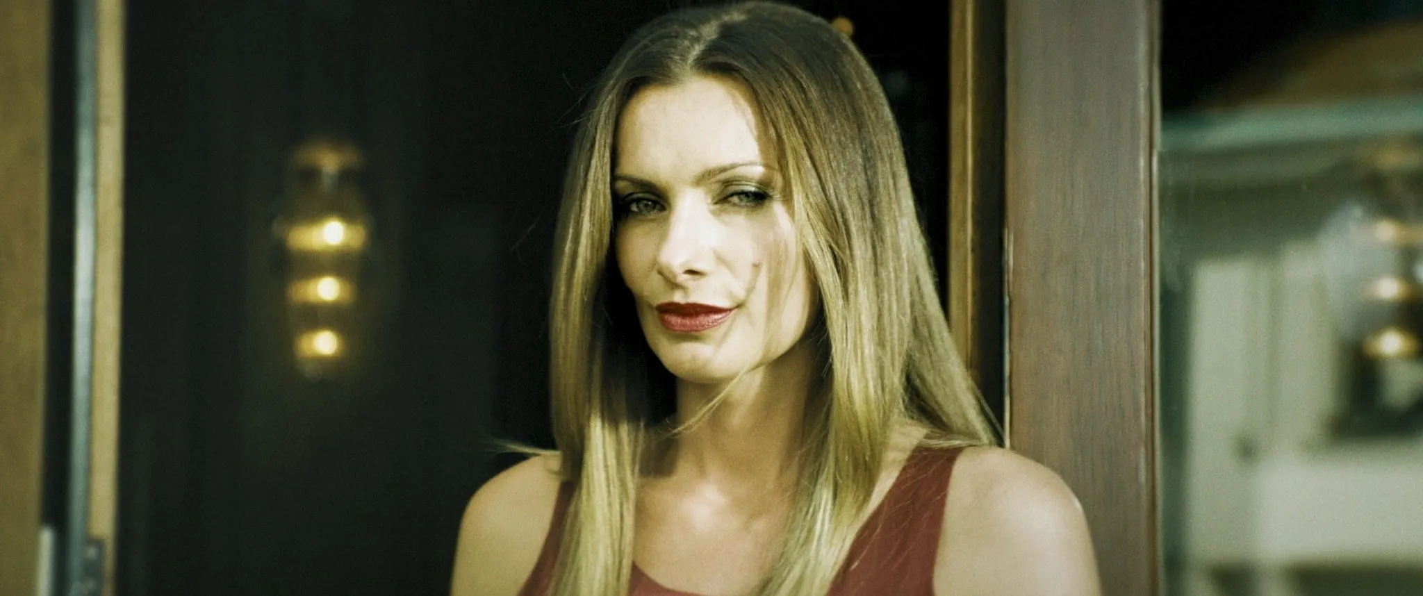Close-up of a blonde woman in a wine-red top with a faint smile and narrowed eyes