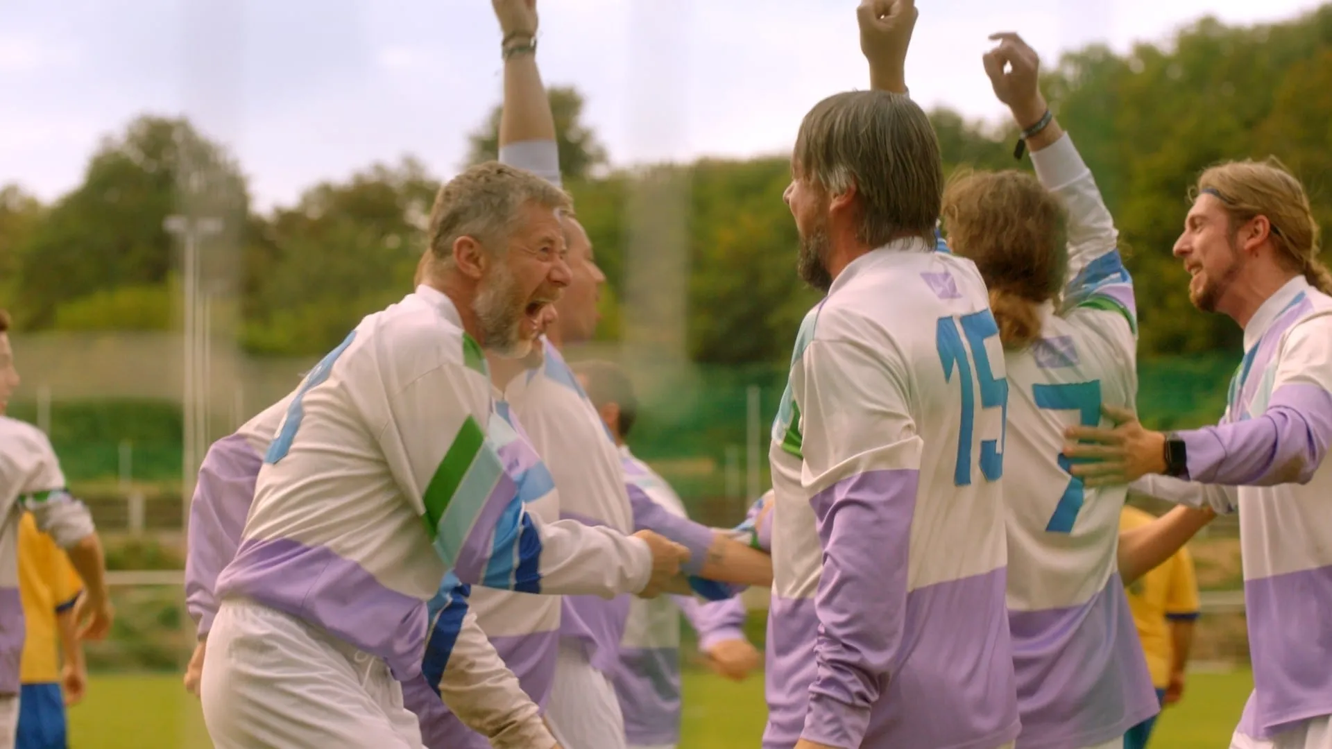 Footballers in white and lilac kits celebrate on the pitch, one of them shouting in triumph