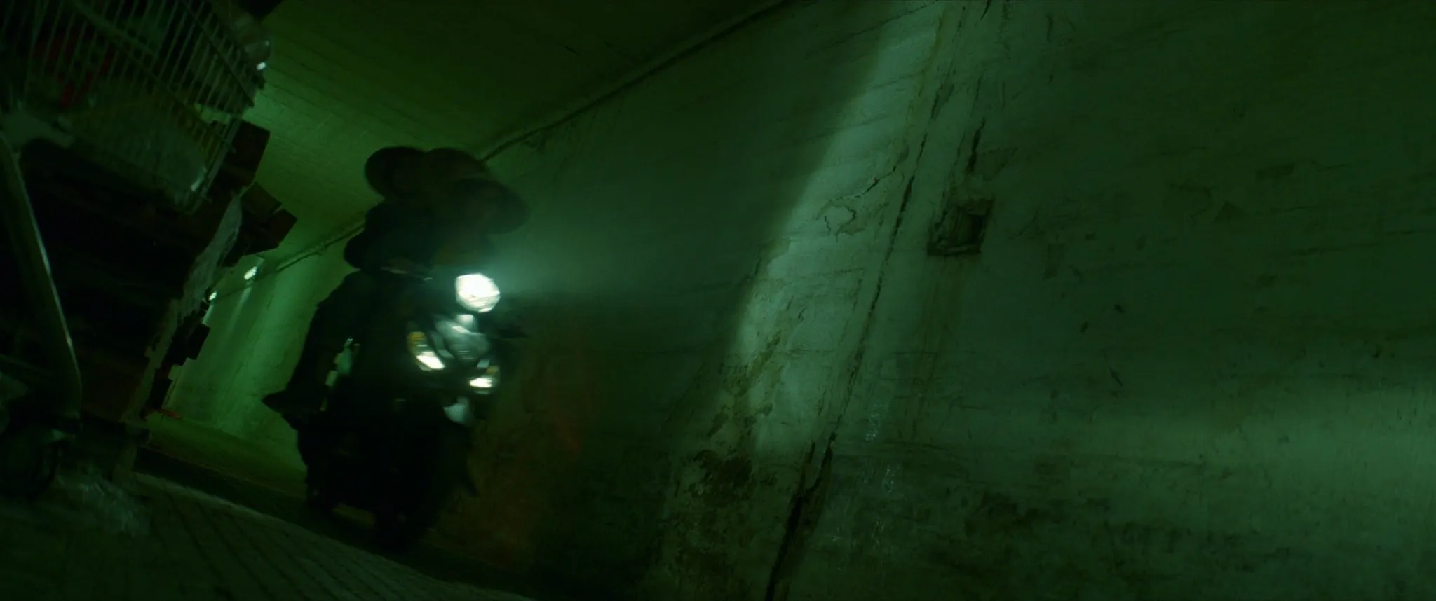 A motorcyclist with the headlight on rides through a dark corridor washed in green light