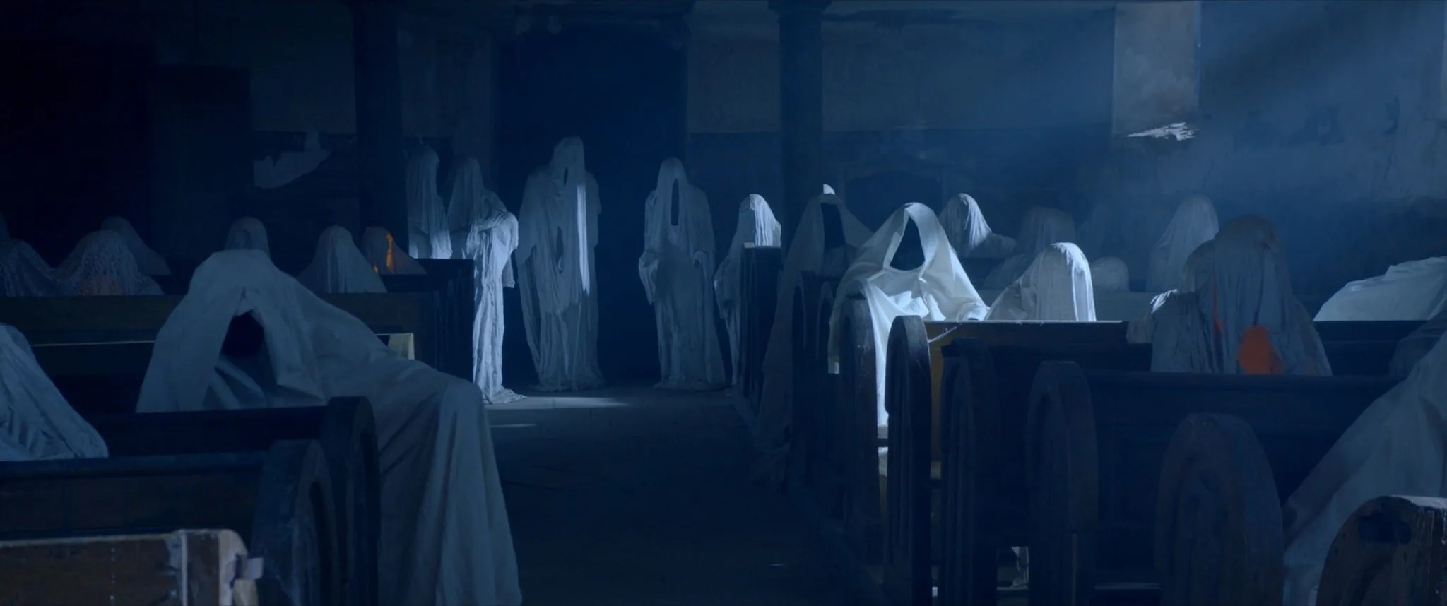 Figures draped like ghosts in white sheets stand and sit among the pews of a dim church